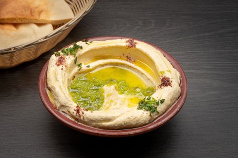 Hummus A bowl of hummus is sitting on a table next to a basket of pita bread.