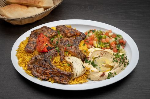 Lamb Chops A plate of food with meat , rice , hummus and vegetables on a table.