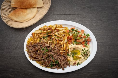 Mix Shawarma Plate A plate of food with meat , rice , hummus and pita bread on a table.