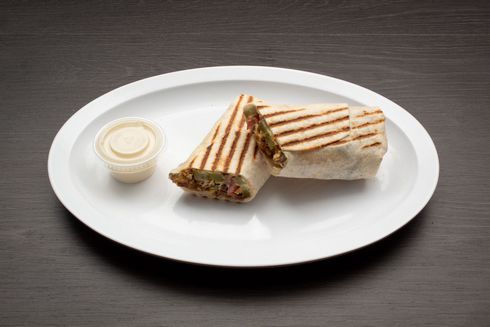 Beef Shawarma A white plate topped with a sandwich and a small cup of sauce.