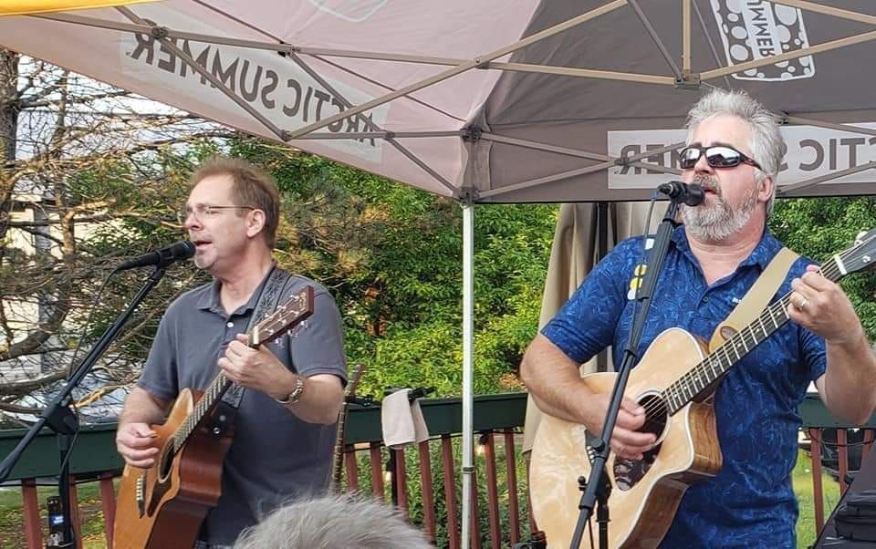 Two men are playing guitars and singing into microphones on a stage.