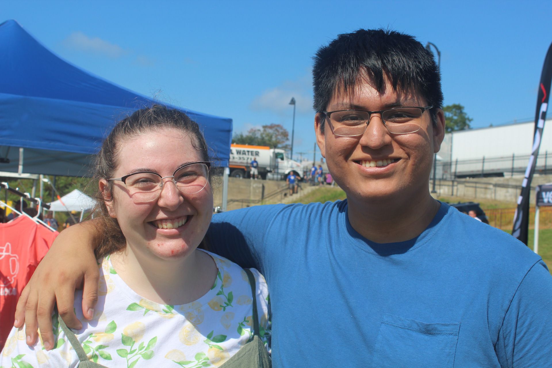 A man and a woman are posing for a picture in front of a blue tent.