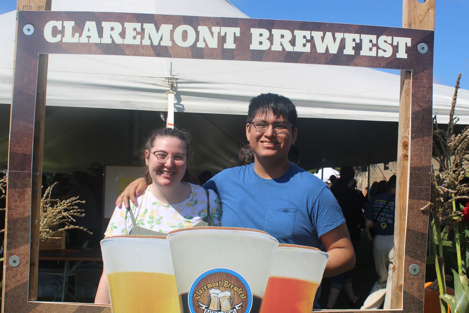 A man and a woman are posing for a picture in front of a sign that says claremont brewfest.