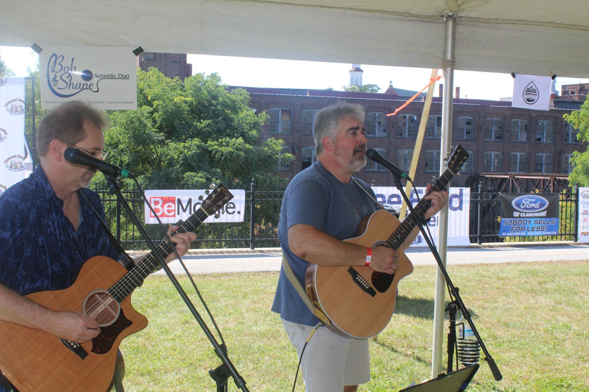 Two men playing guitars and singing into microphones under a tent
