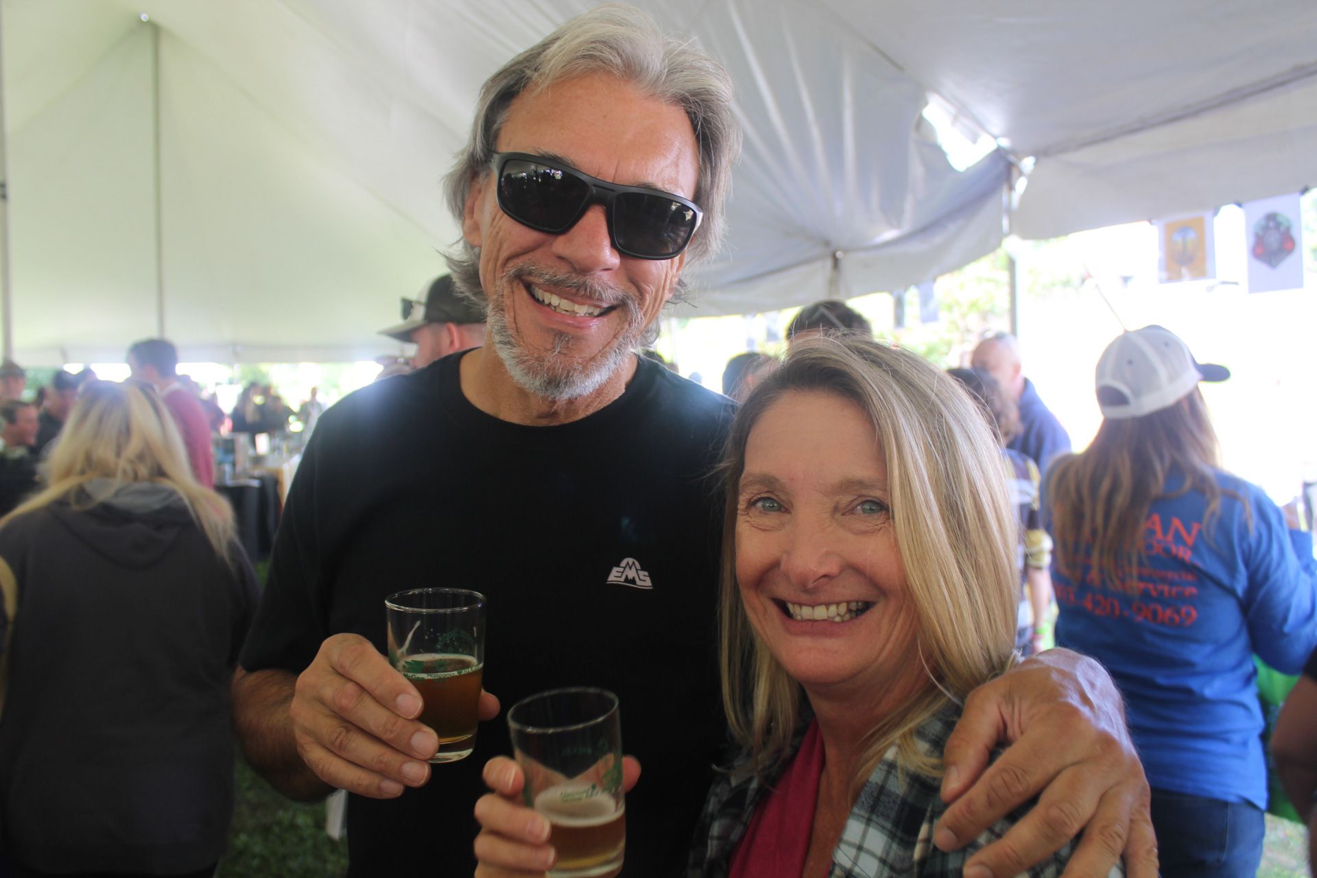 A man and a woman are posing for a picture while holding glasses of beer.
