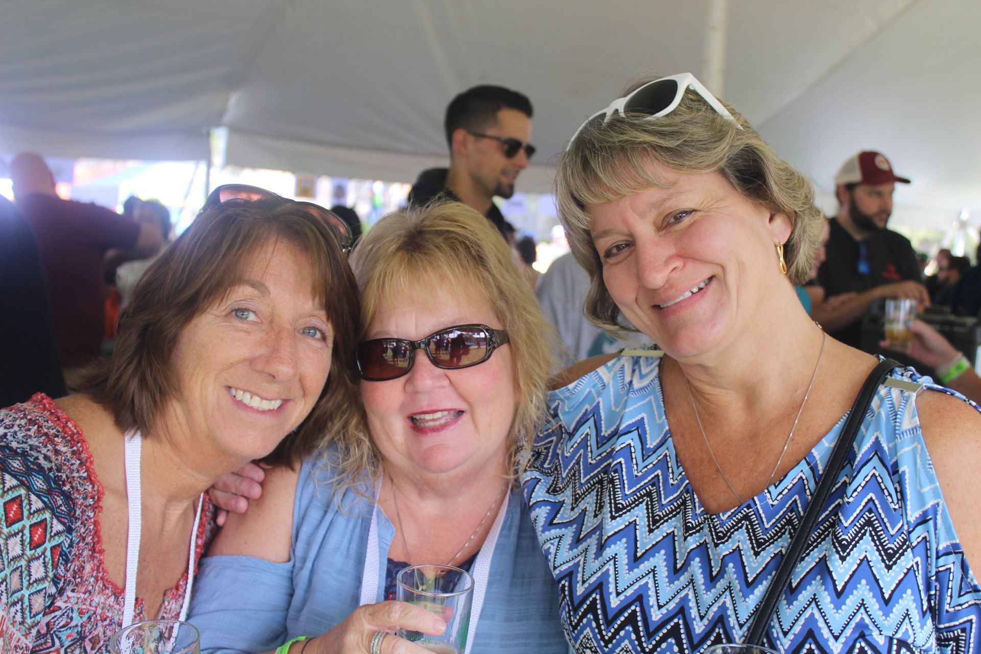 Three women are posing for a picture together under a tent.