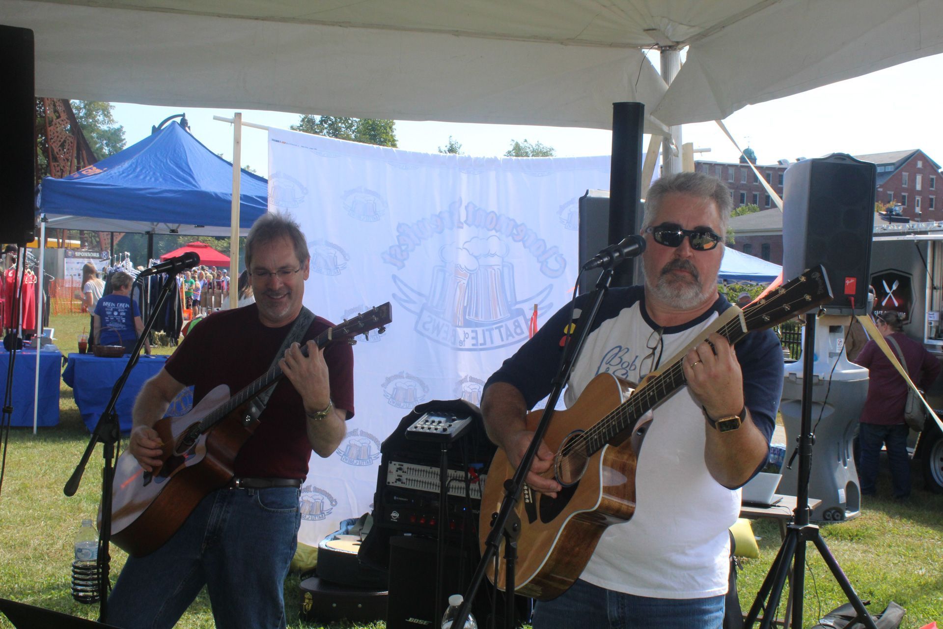 Two men are playing guitars in front of a sign that says 100 years