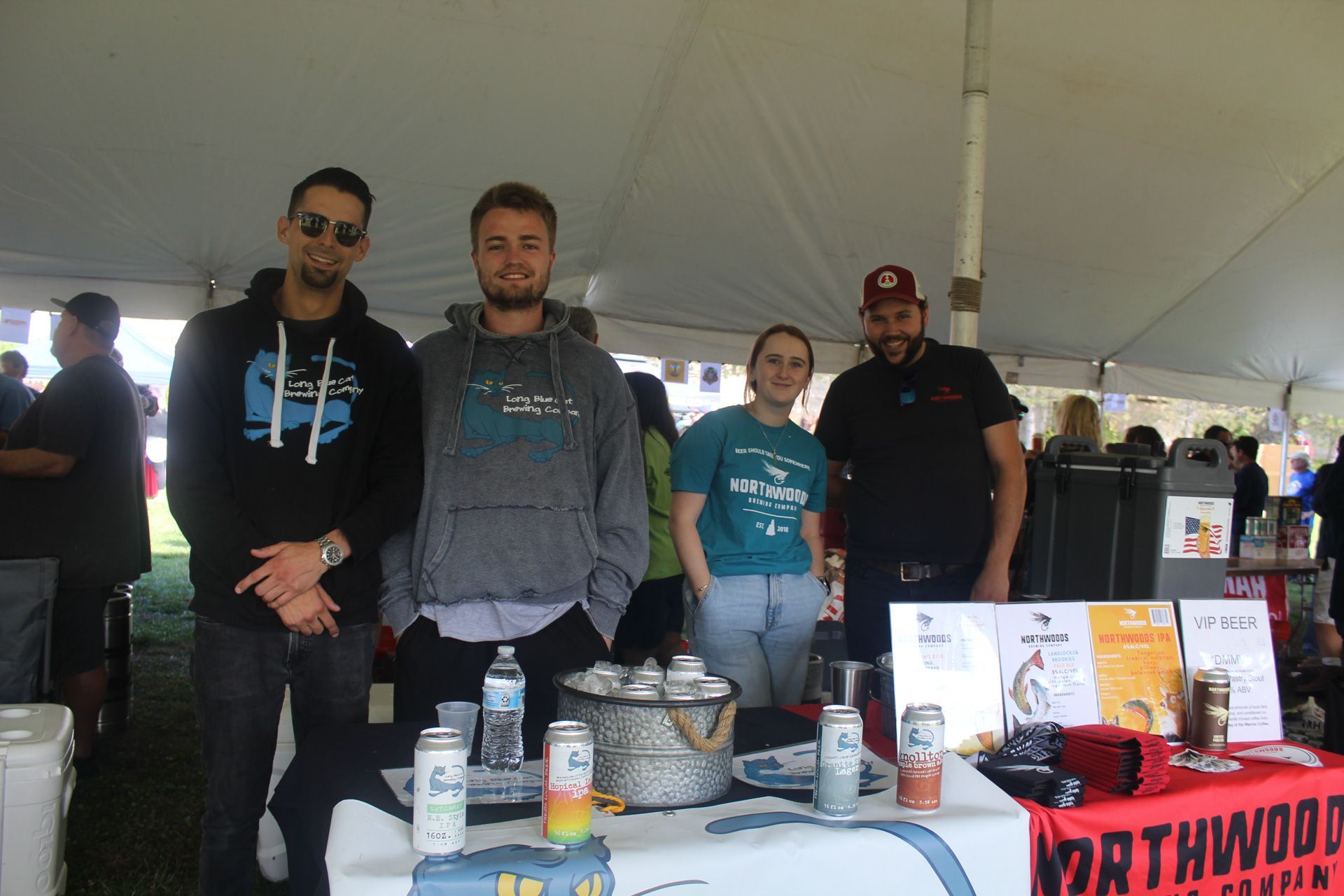 A group of people standing around a table with cans of beer on it.
