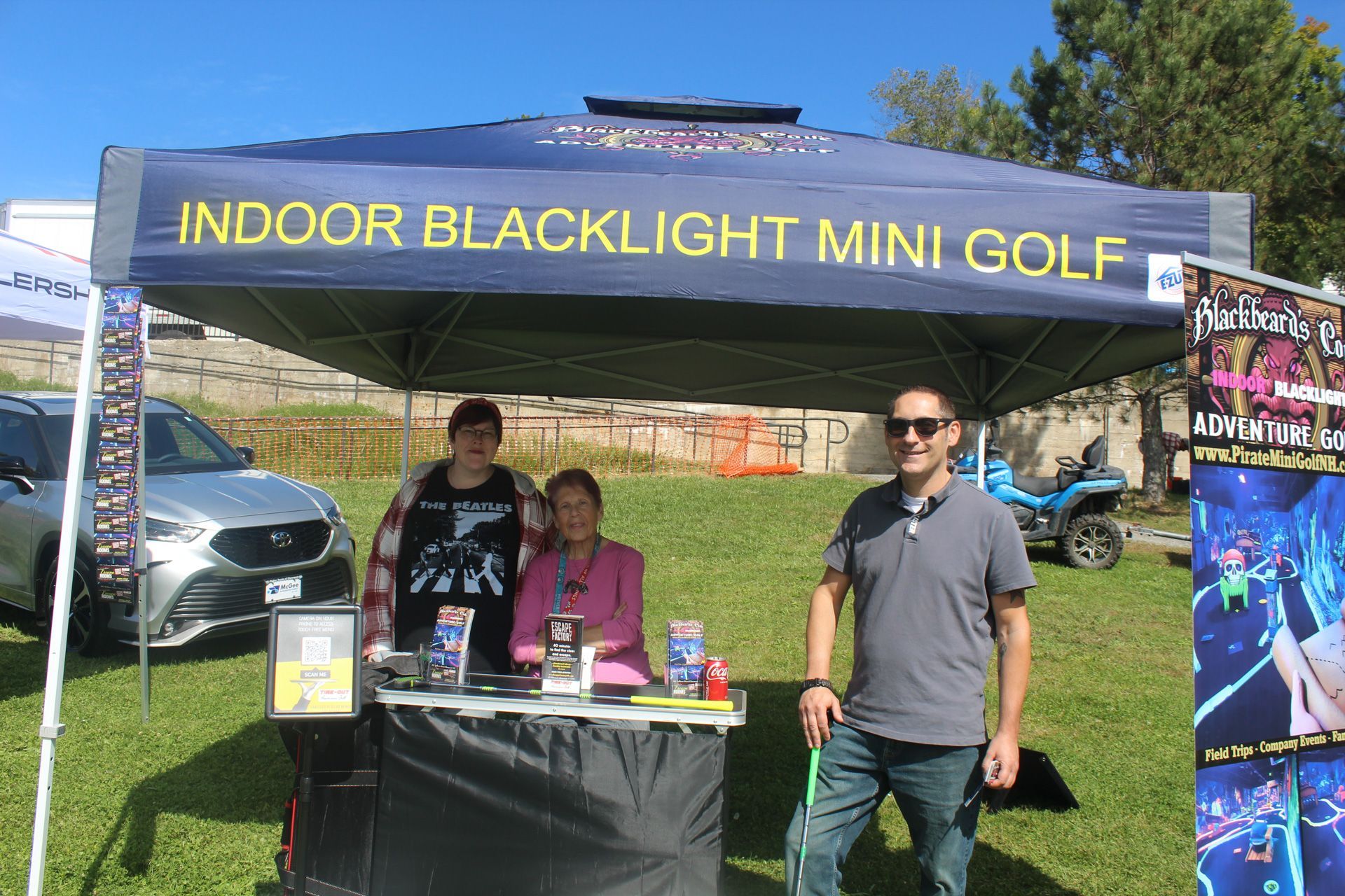 A group of people standing under a tent that says indoor blacklight mini golf