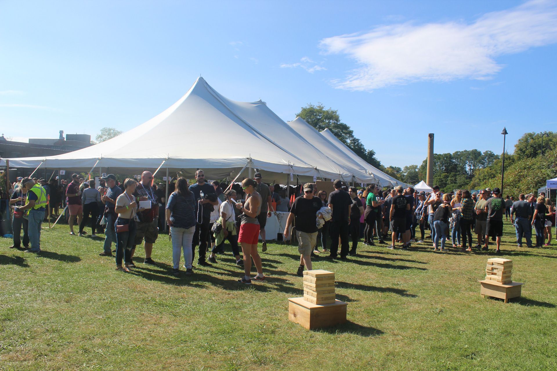 A large group of people are standing in a field under a tent.