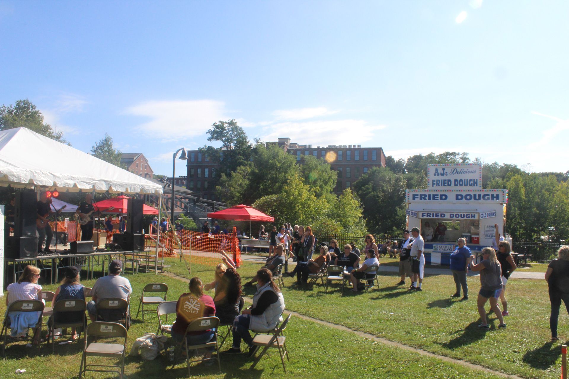 A group of people are gathered in a park in front of a fried dough stand