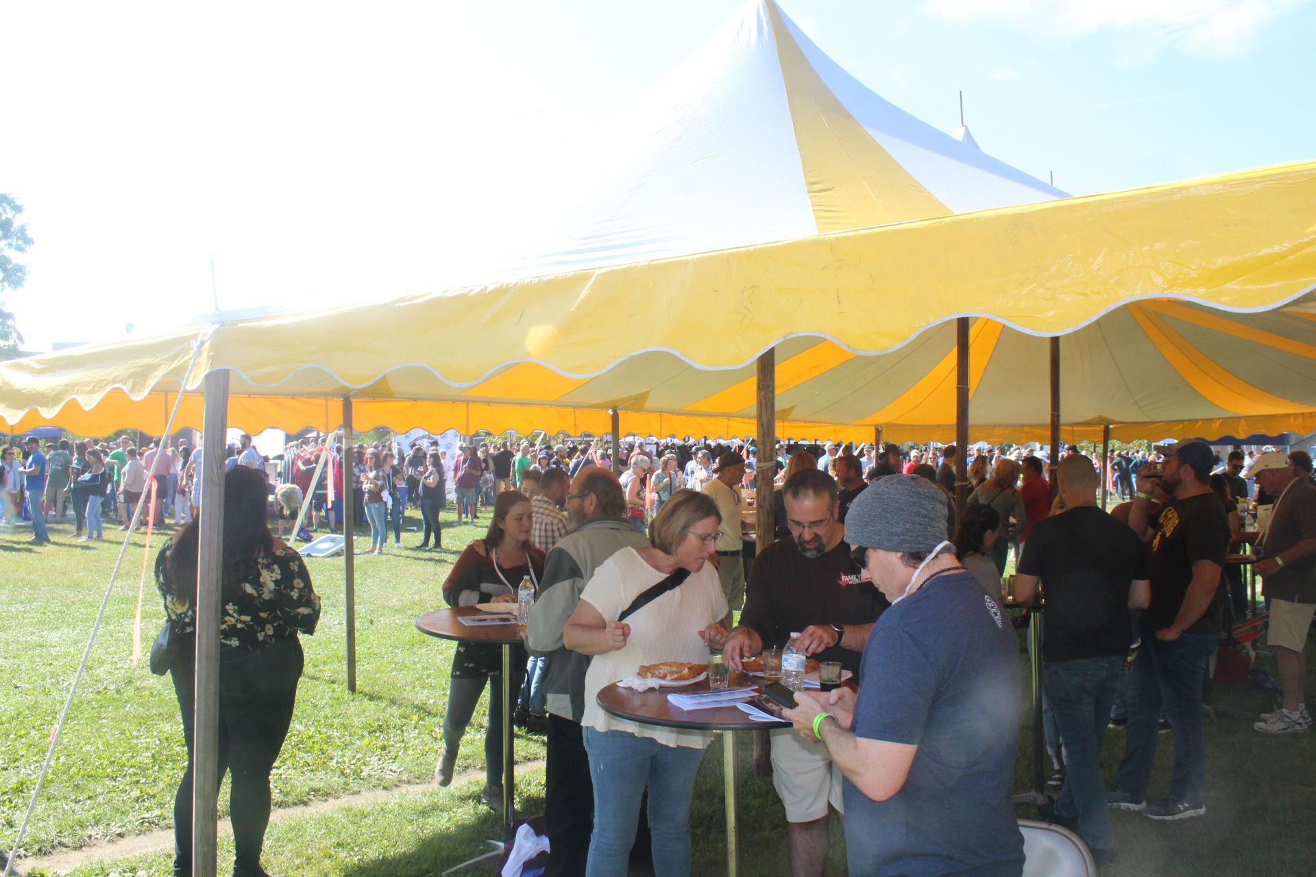 A crowd of people are gathered under a yellow and white tent