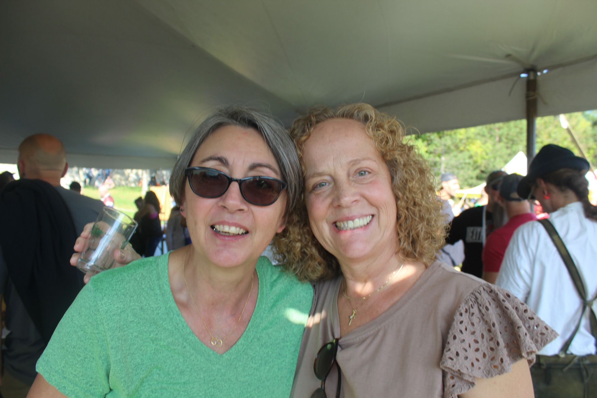 Two women are posing for a picture together under a tent.