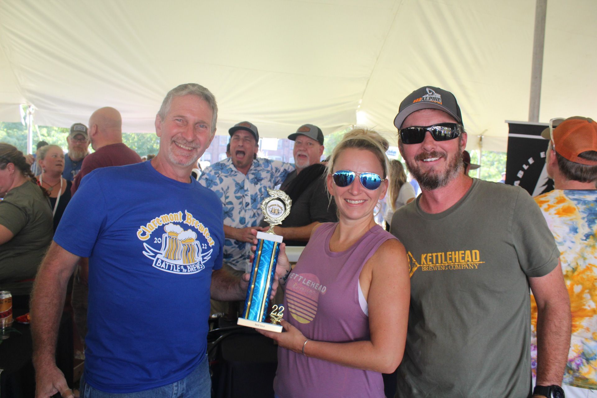 A group of people are standing under a tent holding a trophy.