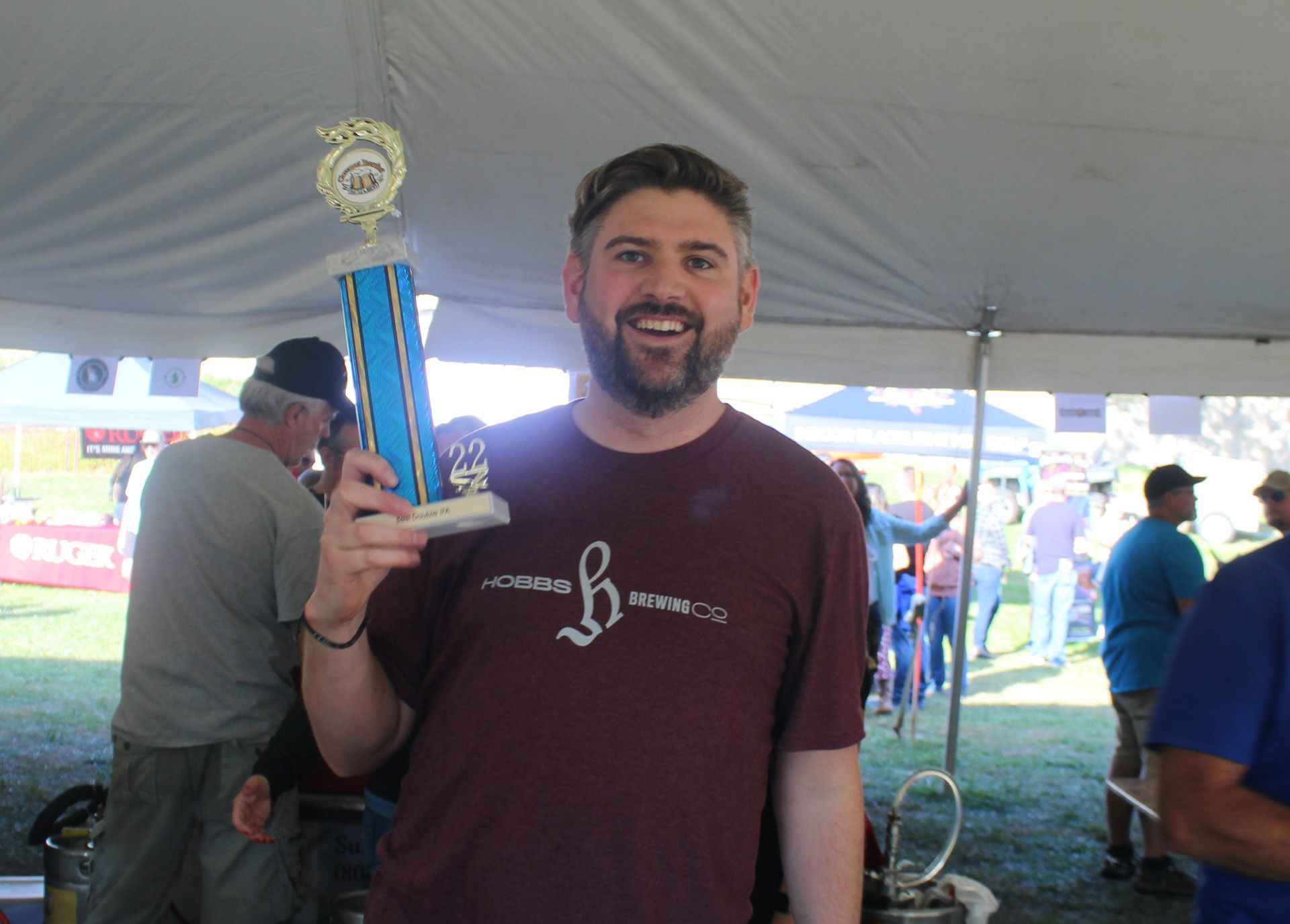 A man in a maroon shirt is holding a trophy