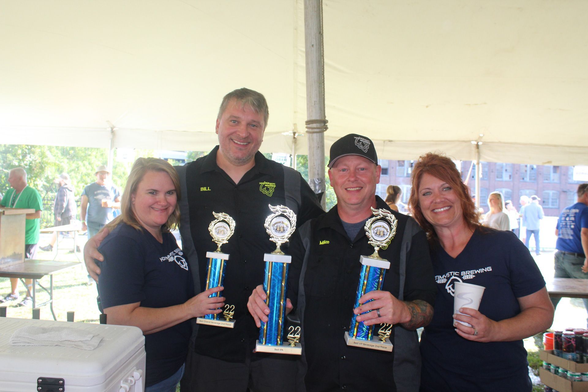 A group of people are standing under a tent holding trophies.