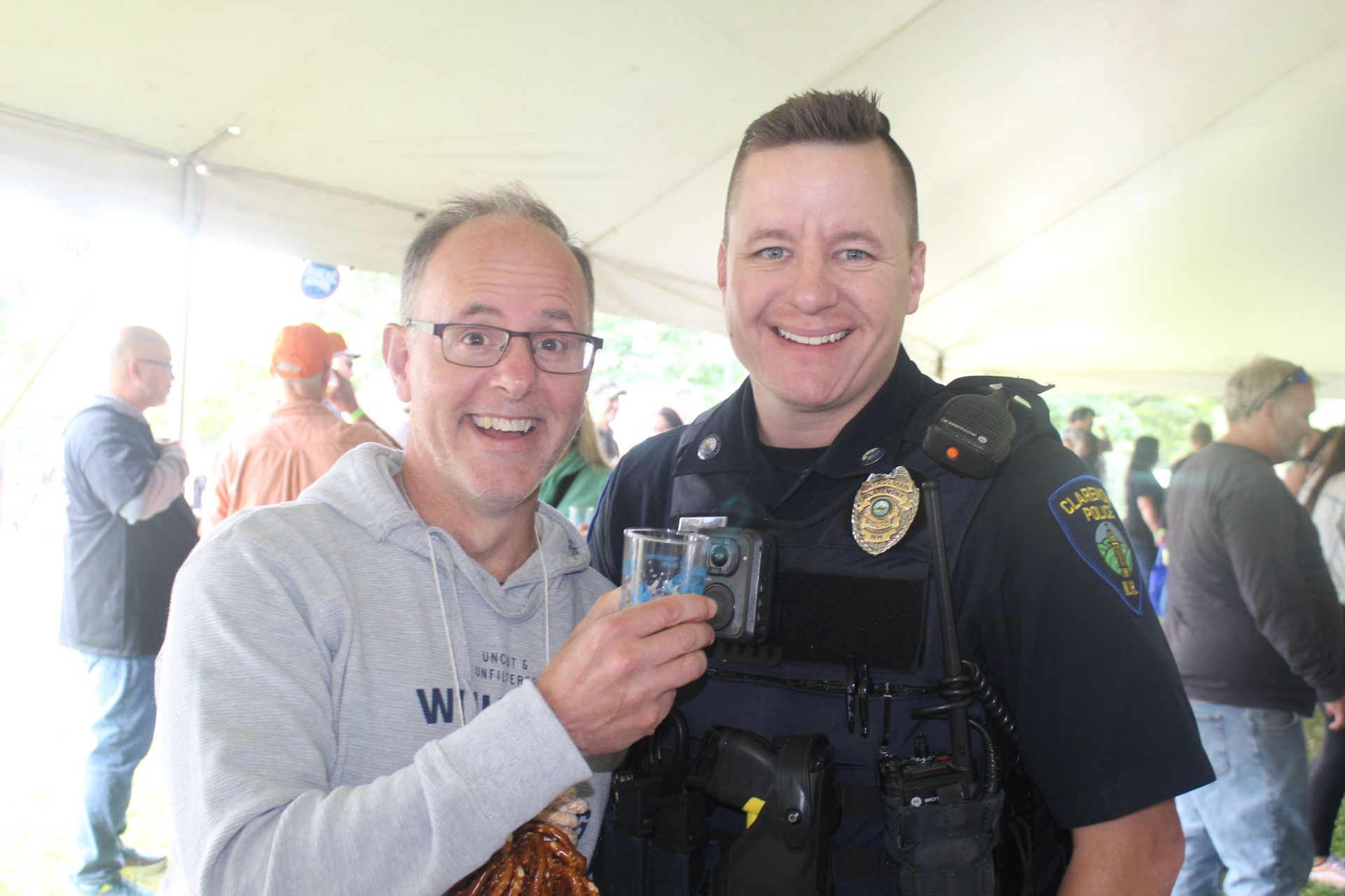 A police officer is standing next to a man holding a glass of beer.
