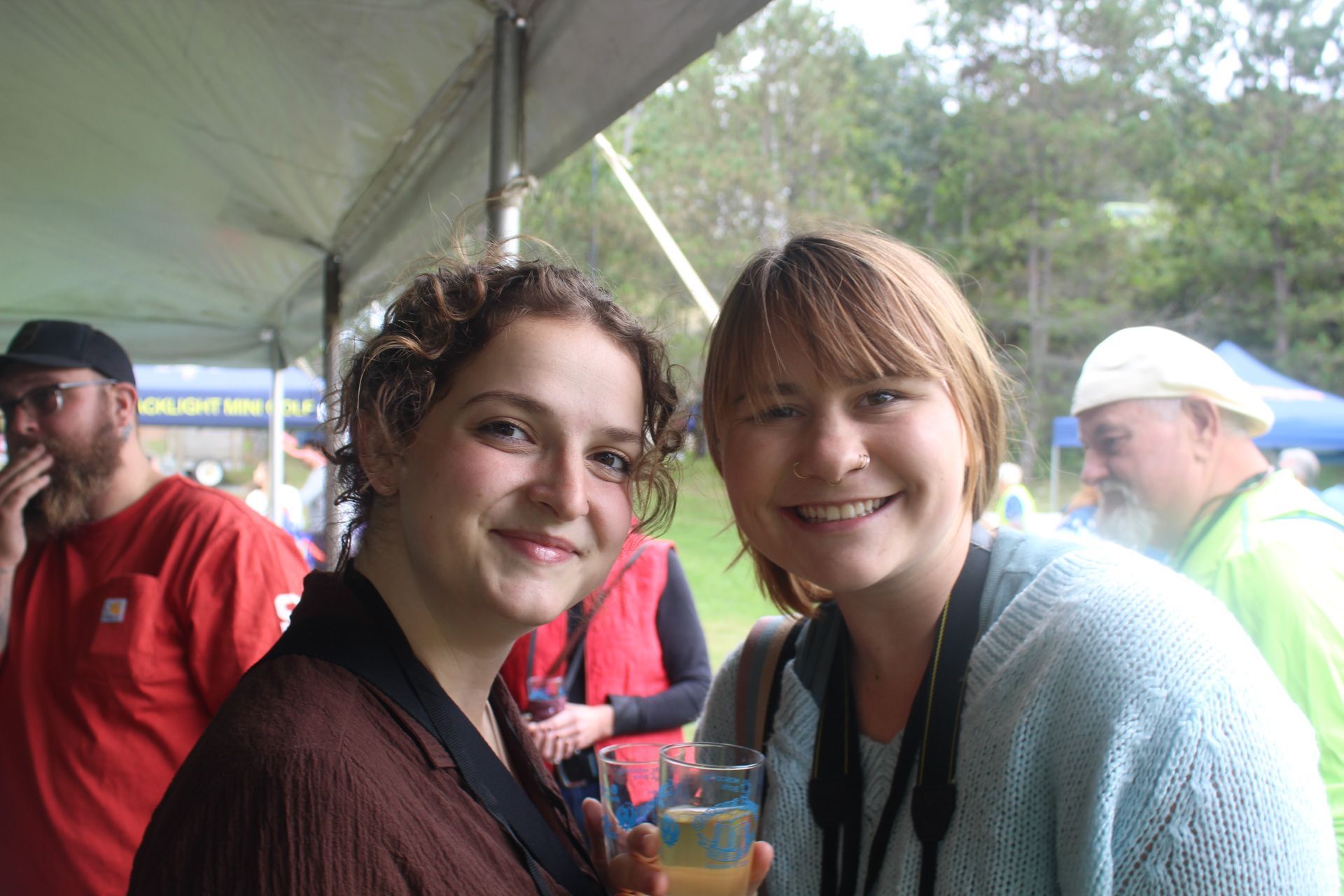 Two women are posing for a picture while one of them is holding a glass of wine.