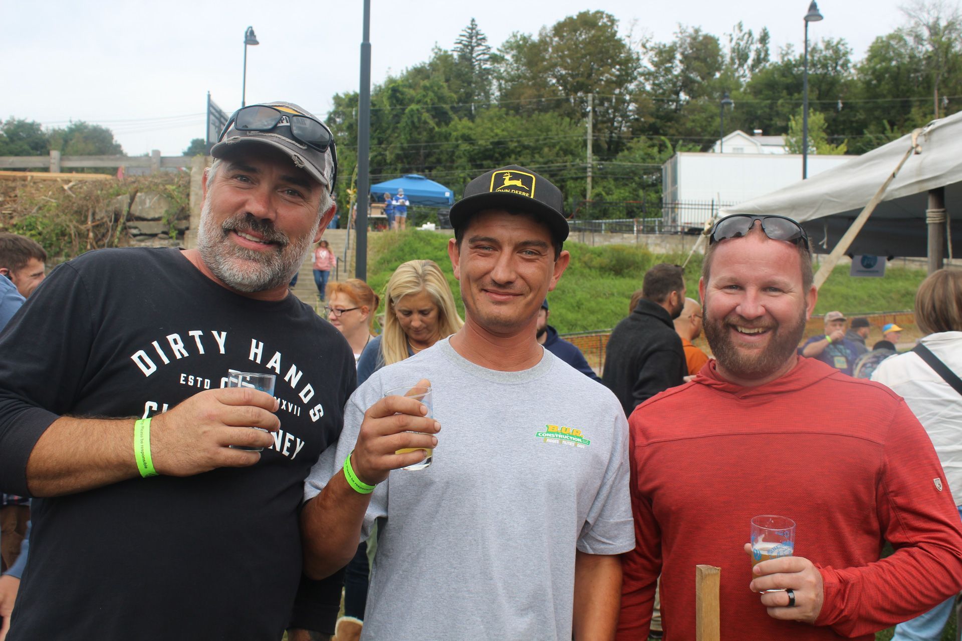 Three men are standing next to each other holding glasses of beer.