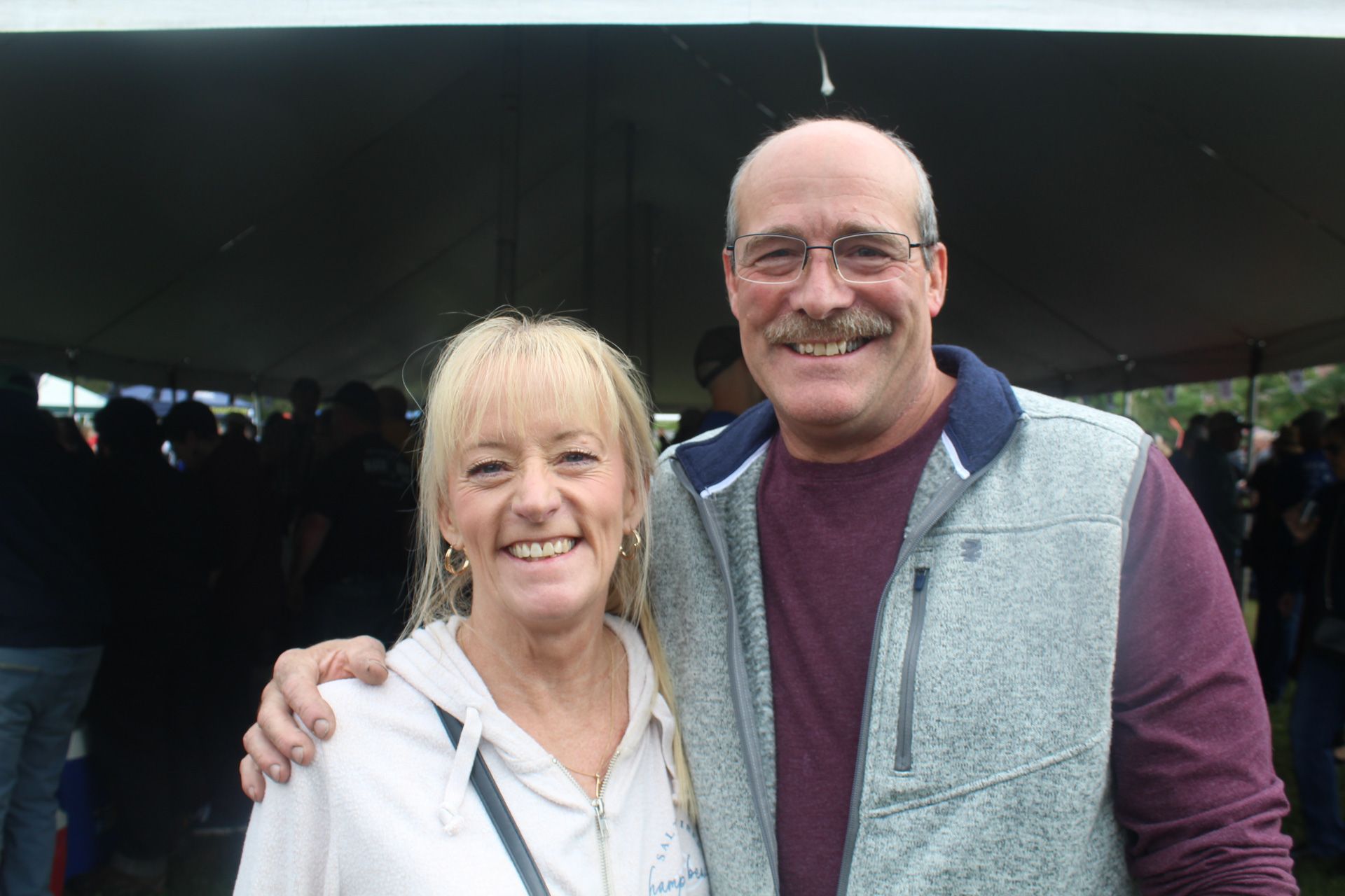 A man and a woman are posing for a picture under a tent.
