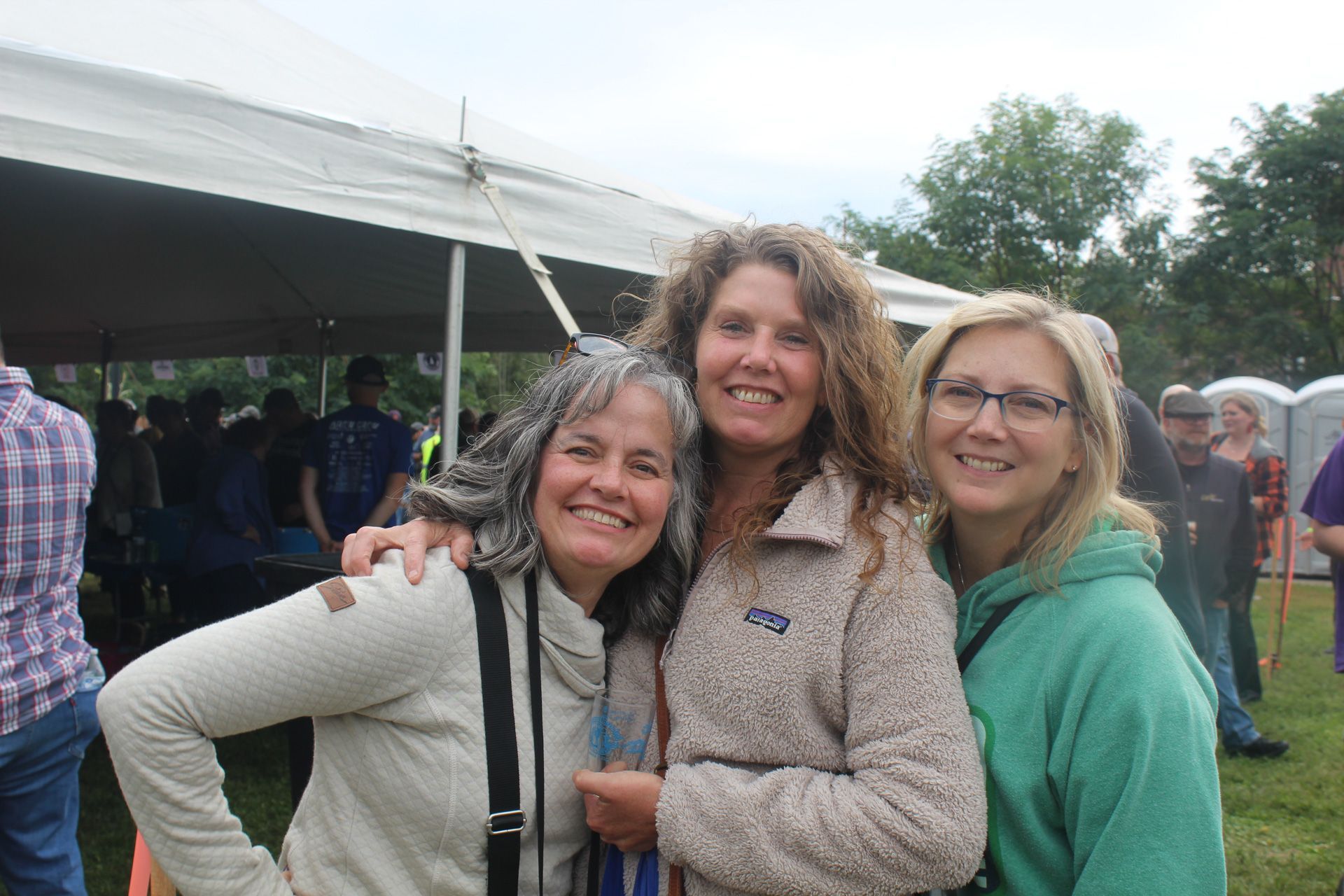 Three women are posing for a picture in front of a tent.