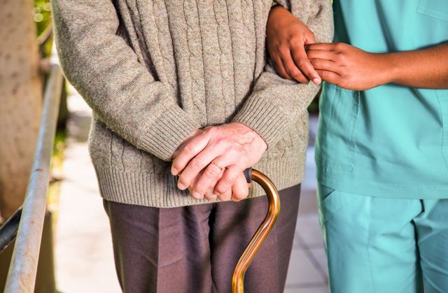 Un uomo anziano con un bastone viene aiutato da un'infermiera.