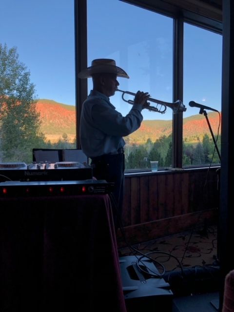 A man in a cowboy hat is playing a trumpet in front of a window