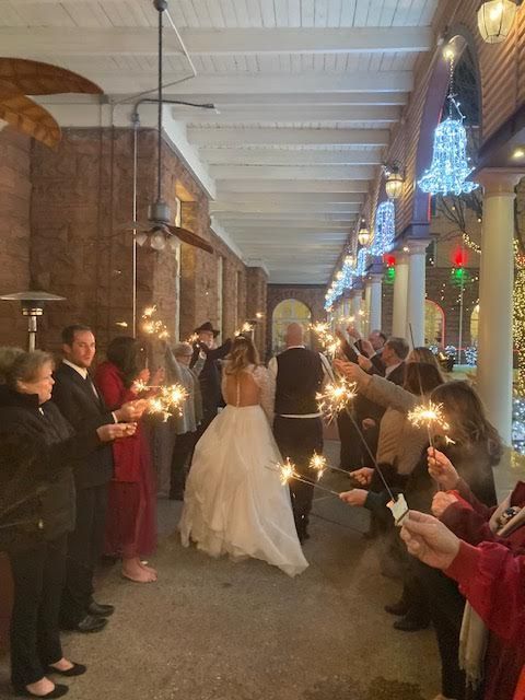 A bride and groom are walking through a crowd of people holding sparklers.