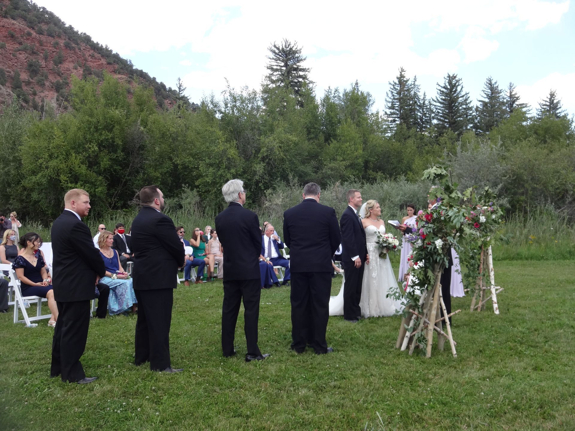 A bride and groom are getting married in a field with a mountain in the background.