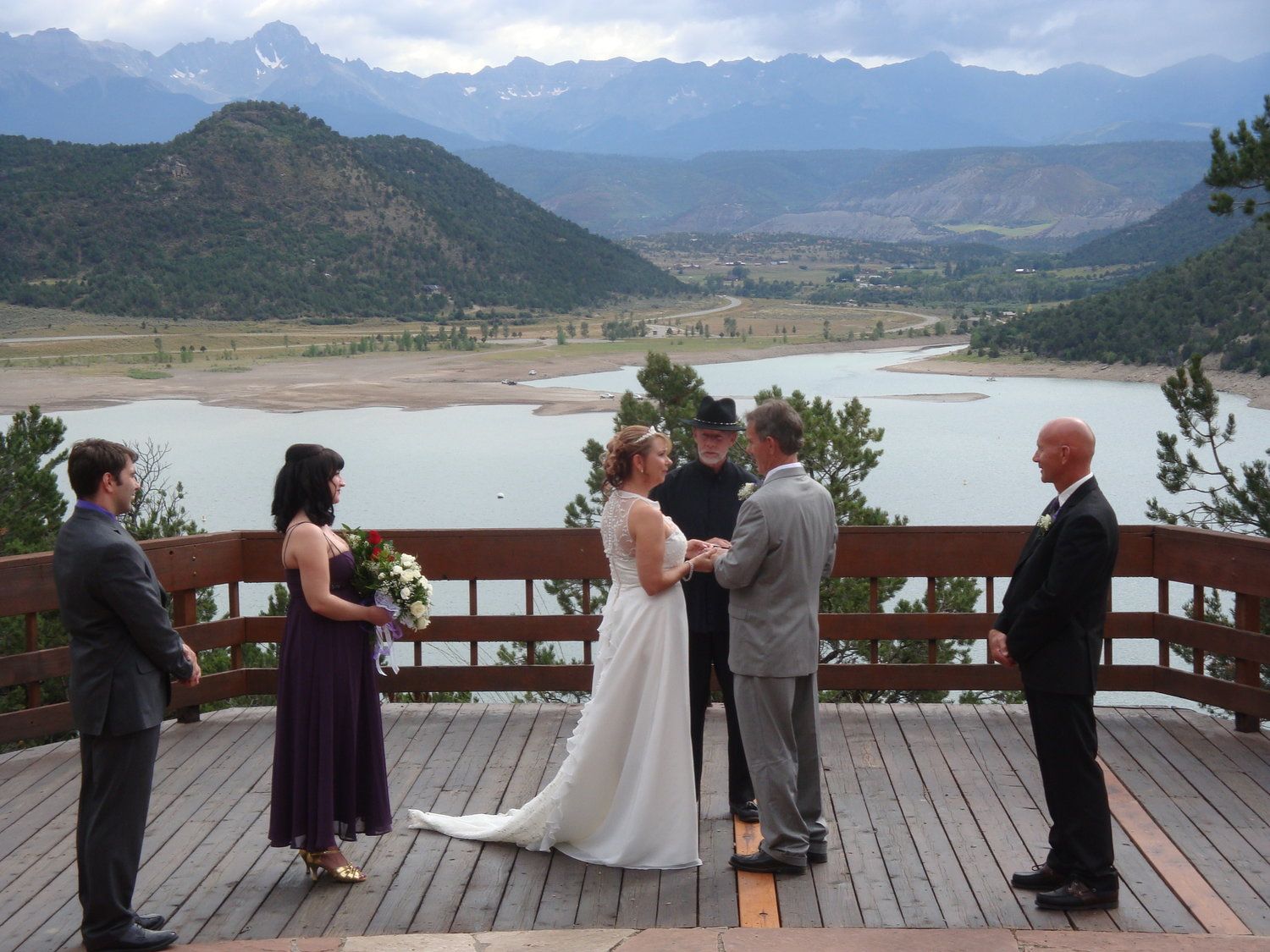 A bride and groom are getting married on a deck overlooking a lake