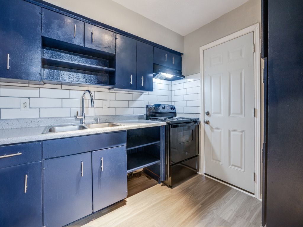 A kitchen with blue cabinets , a stove , a sink , and a door.