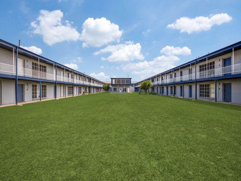 A row of apartment buildings with a large lawn in front of them.