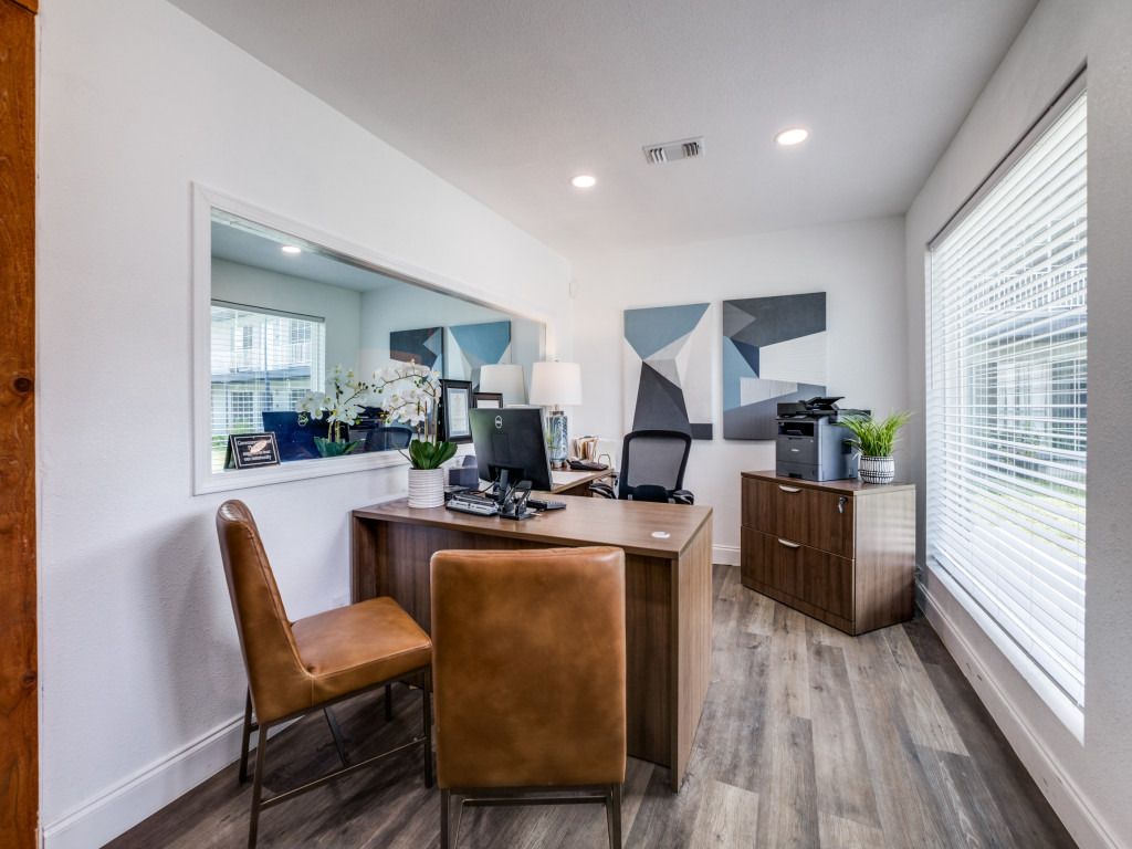 A home office with a desk , chairs , and a large window.