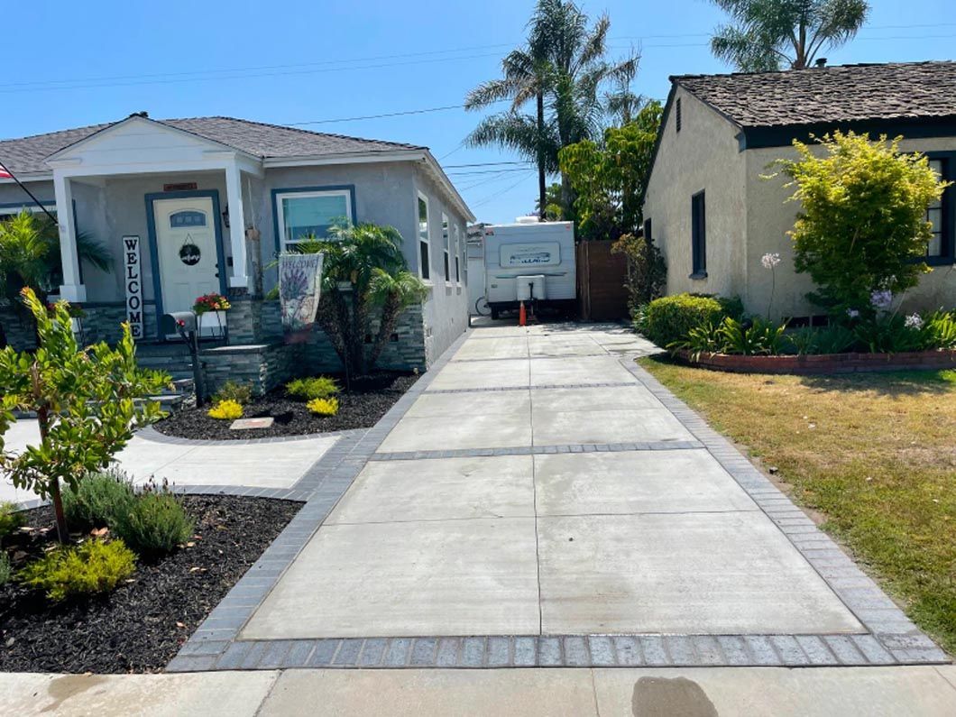 A concrete driveway leading to a house with a trailer parked in front of it.