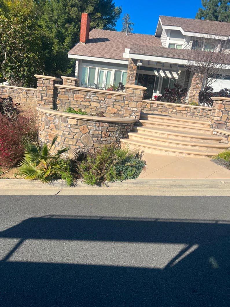 A large house with a stone wall and stairs is on the side of the road.