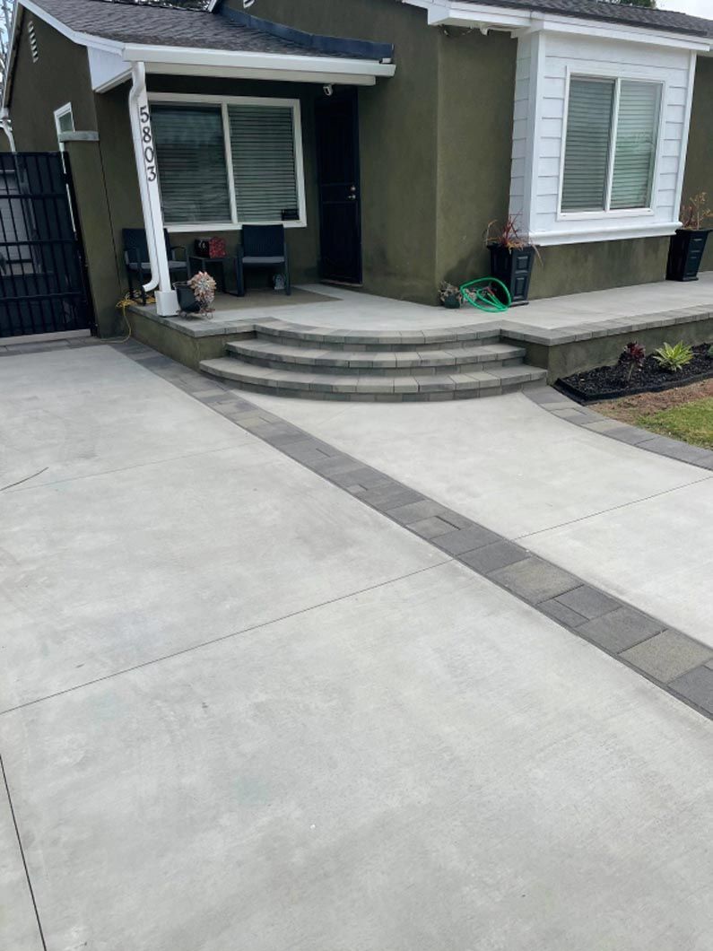 A concrete driveway leading to a house with stairs and a porch.