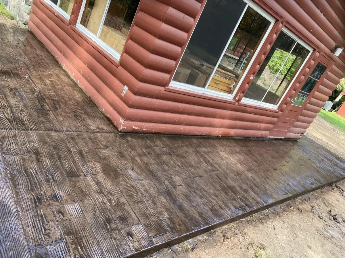 Wooden deck beside a log cabin with large windows and a weathered surface