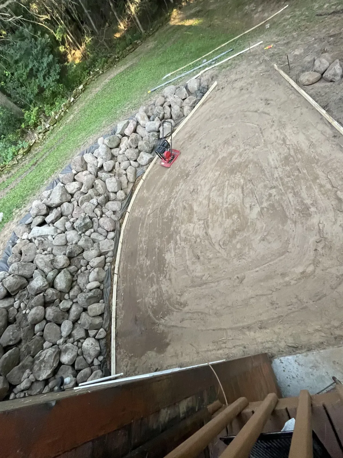 Curved concrete patio beside a rock-lined path and grassy yard, viewed from a doorway or deck.