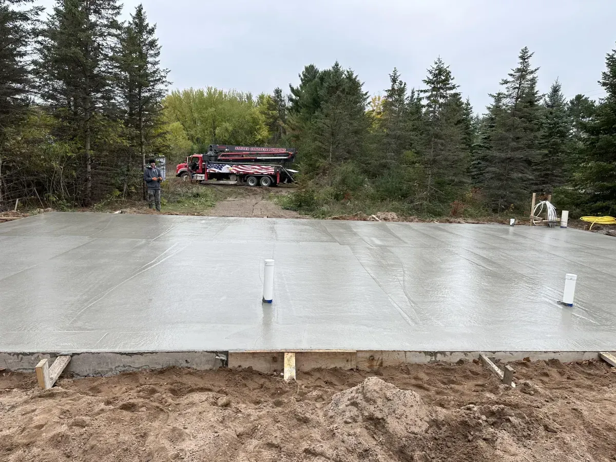 Fresh concrete foundation slab in a wooded area with a red truck in the background