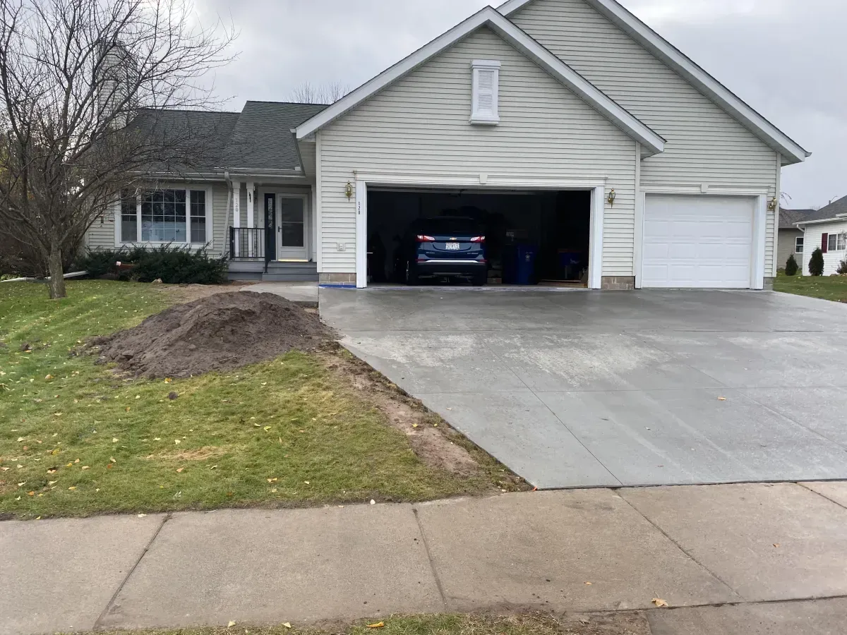 Suburban house with open garage, concrete driveway, and a pile of dirt on the front lawn.