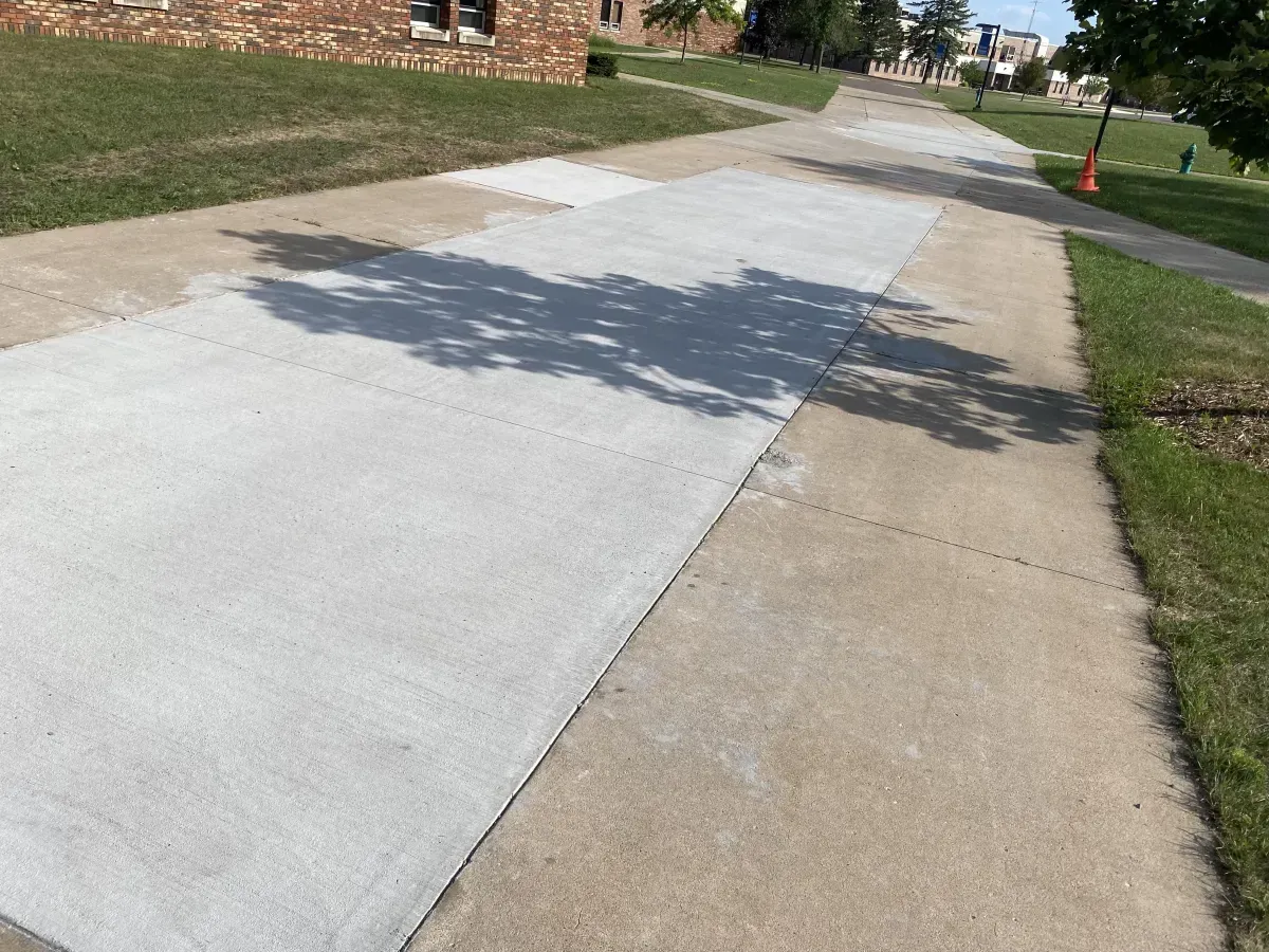 Sidewalk with fresh light-gray concrete beside an older tan walkway in a suburban neighborhood