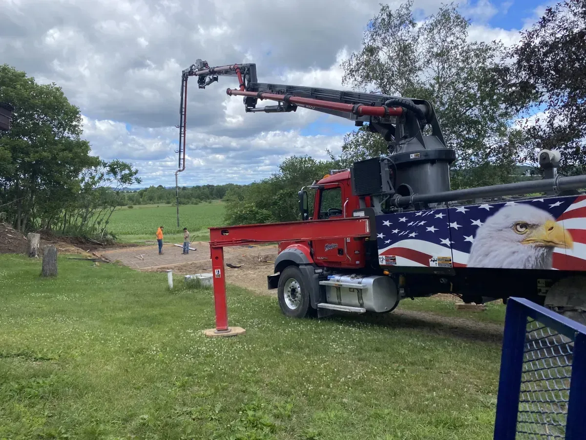 Red crane truck hoists a hanging chain beside a grassy road under cloudy sky