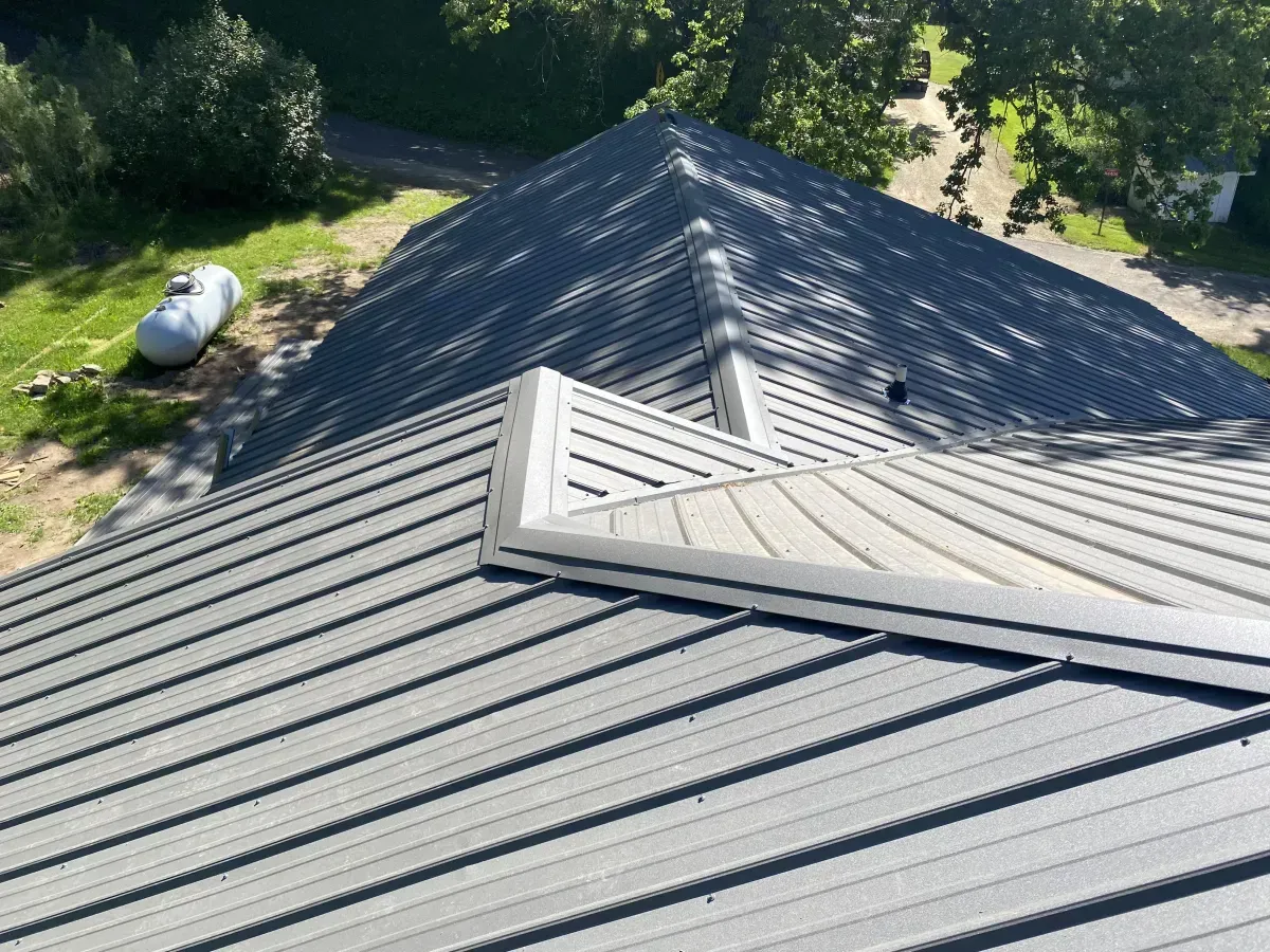 Gray metal roof with a small skylight, viewed from above near trees and a grassy yard