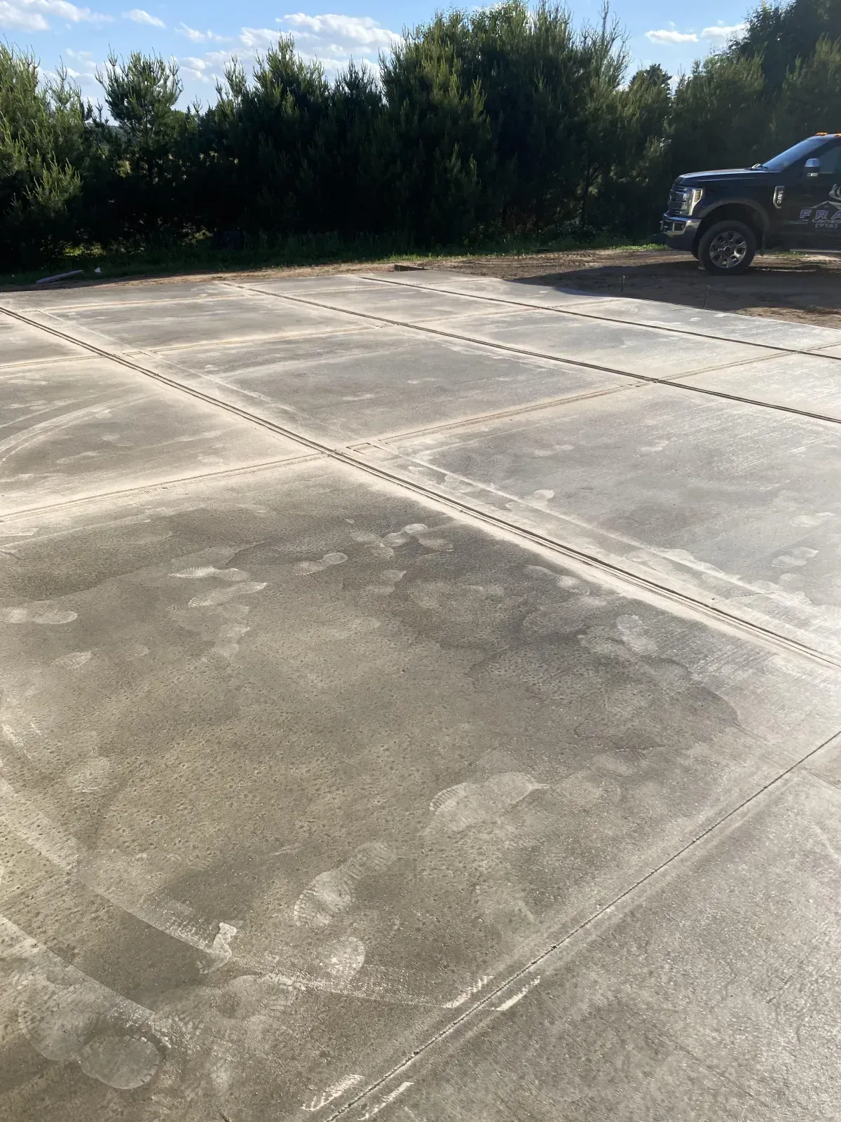 Concrete parking lot with a black SUV at the edge and trees in the background