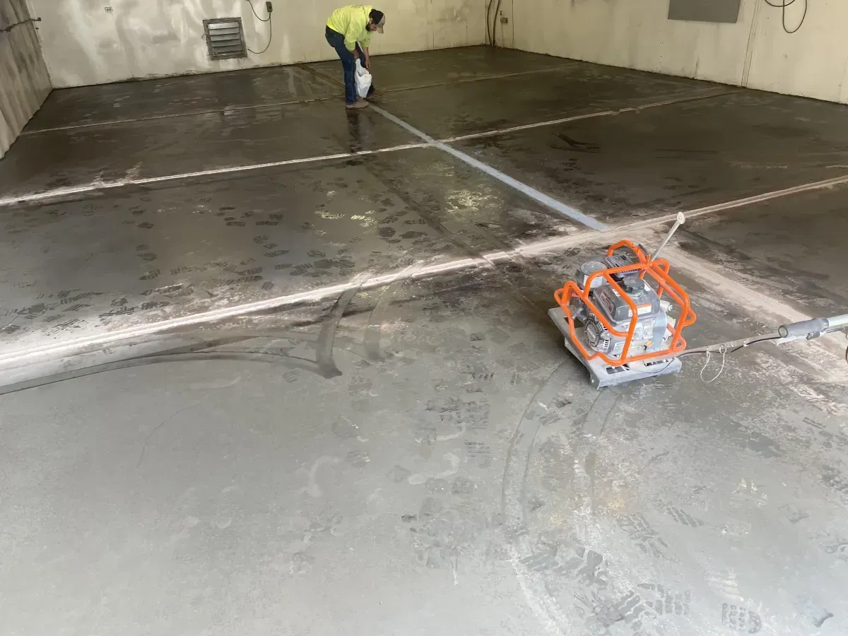Worker smoothing wet concrete floor with a power trowel in a large industrial space