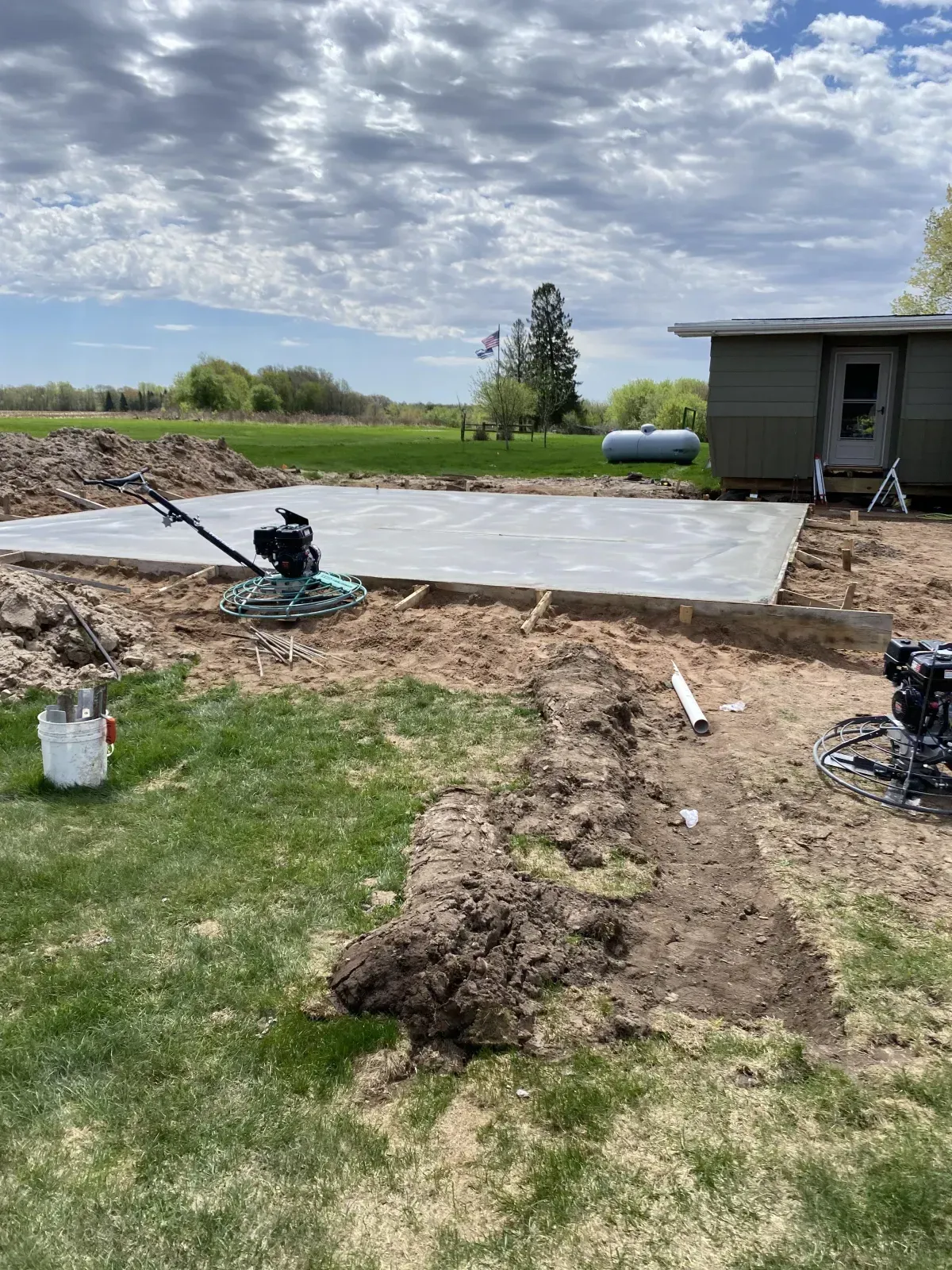 Backyard construction site with a partially cleared yard, tarp, dirt piles, and a small building nearby