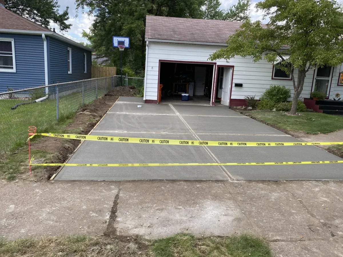 Driveway under construction with wet concrete and yellow caution tape in front of an open garage.