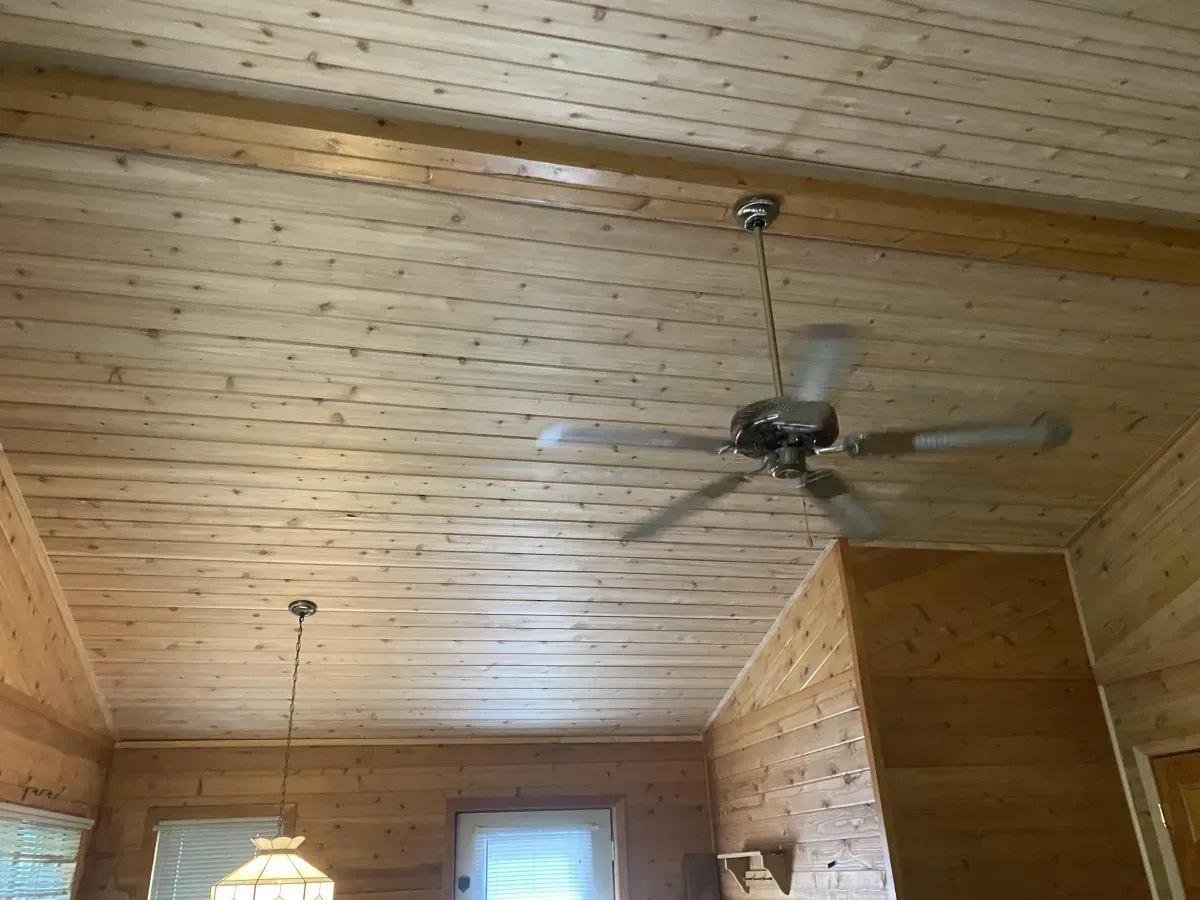 Wood-paneled room with a sloped wood ceiling, ceiling fan, hanging light, and windows.