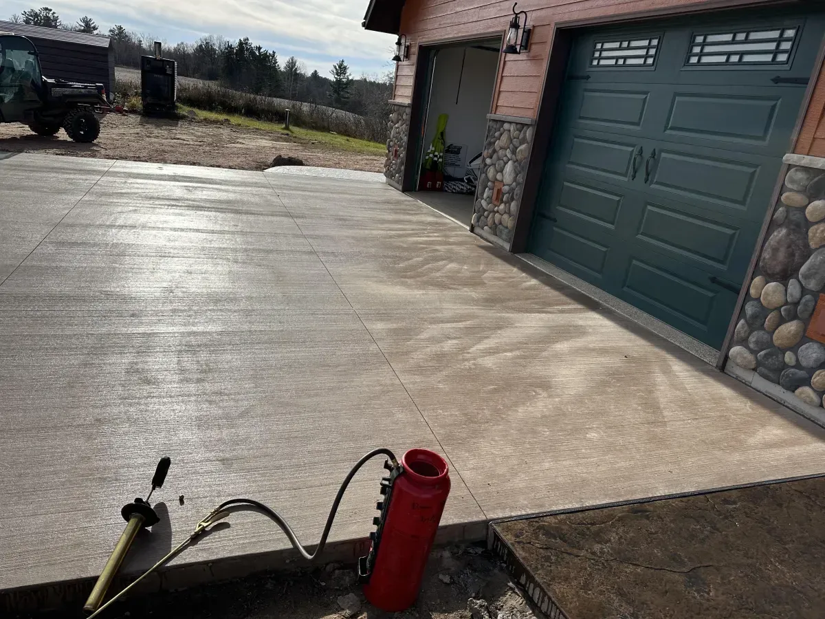 Concrete driveway beside a garage with a red thermos in the foreground and a bright, overcast sky.