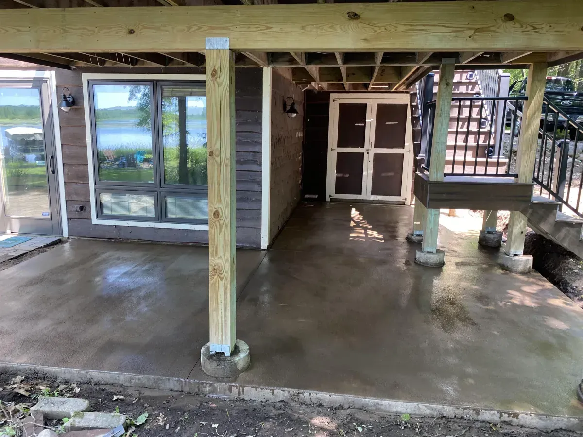 Covered porch with concrete floor, wooden posts, and sliding glass doors overlooking water.